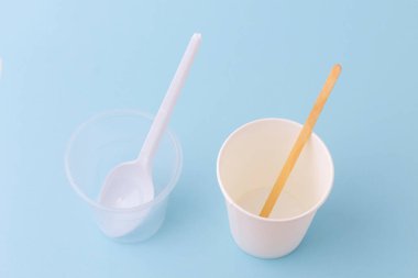 Tek kullanımlık plastik sofra takımı: fincan ve kaşık. Çevre dostu tek kullanımlık eşyalar: kağıt bardak ve tahta kaşık. Plastik kullanmama kavramı. Mavi arkaplan