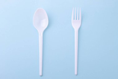 Plastic disposable fork and spoon on a blue background clipart