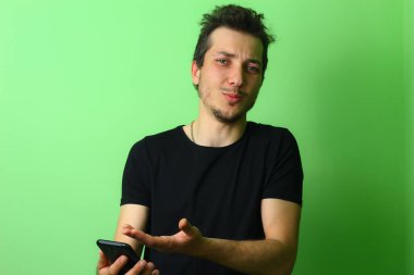Genç hoşnutsuz adam, yeşil bir arka planda hoşnutsuzluk duygularını ifade eder.