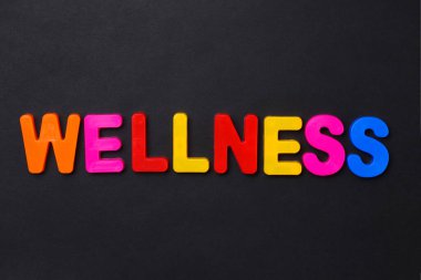 WELLNESS kelimesi çocukların manyetik alfabesiyle siyah bir arkaplanda yazılmış.