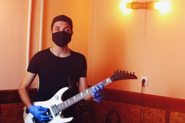 Bir müzisyen, bir ses stüdyosundaki müzik aletinde eldivenle çalar. Covid-19 salgınında bir gitaristin hayatı.
