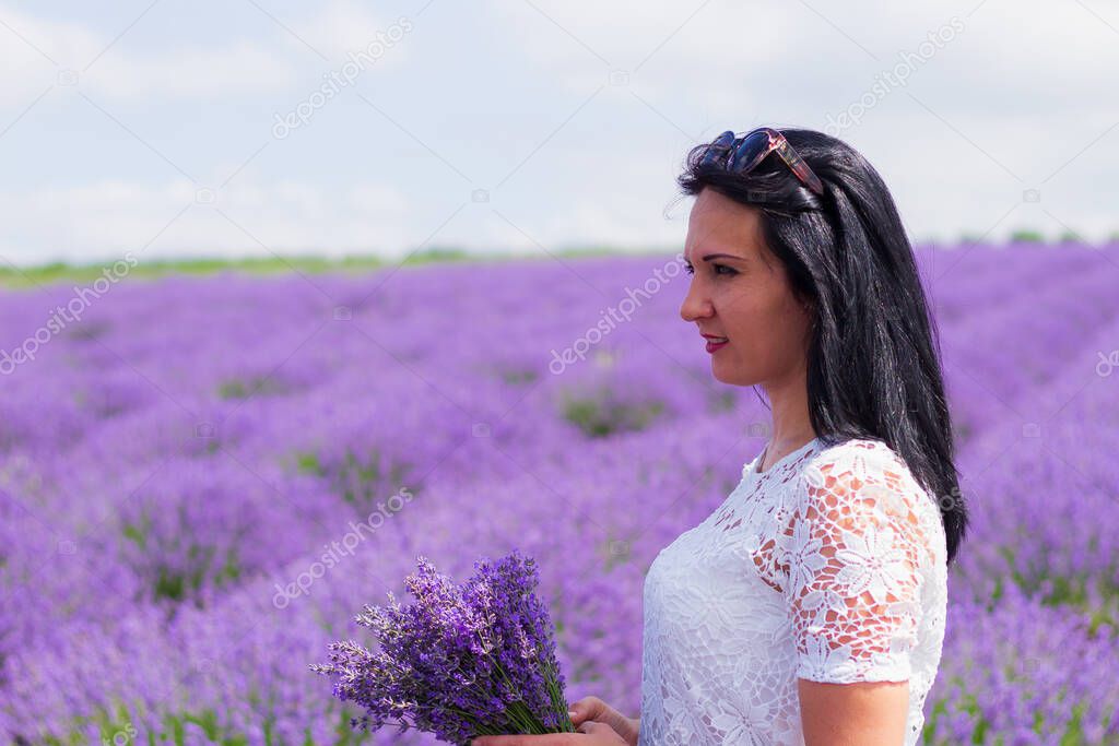 A young brunette woman of European appearance dressed in light casual clothes in a lavender field. Delight in smell and aroma. Lifestyle. Solitude with nature