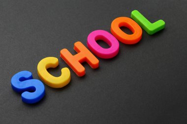 Çok renkli manyetik harflerle yazılmış bir metin. OKULU. Siyah arka plan. Seçici odak