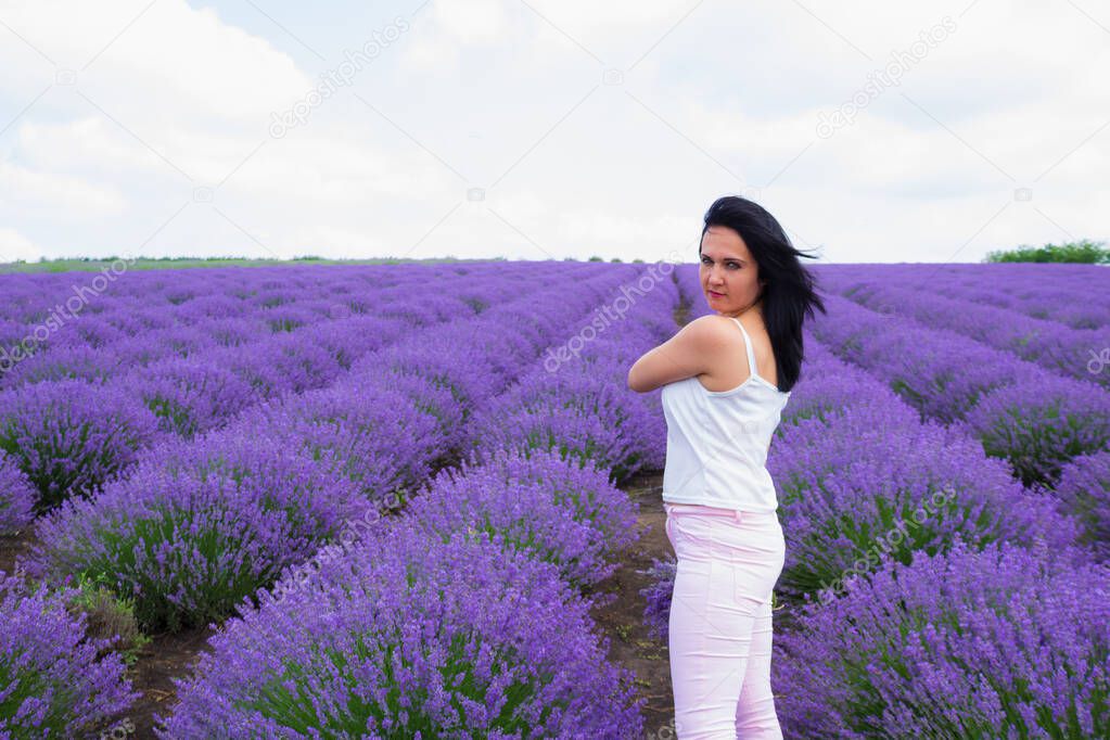 A young brunette woman of European appearance dressed in light casual clothes in a lavender field. Delight in smell and aroma. Lifestyle. Solitude with nature