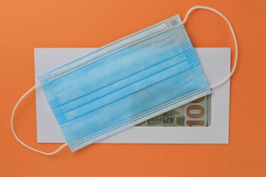 İçinde dolar olan klasik beyaz posta zarfı ve turuncu bir arka planda tıbbi maske. Metin veya harf için boşluk kopyala.