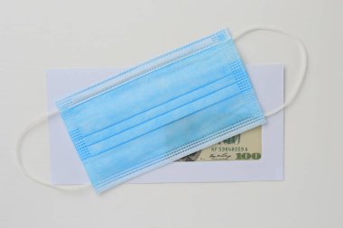 İçinde dolar olan klasik beyaz posta zarfı ve beyaz ahşap arka planda tıbbi bir maske. Metin veya harf için boşluk kopyala.