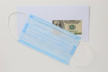 İçinde dolar olan klasik beyaz posta zarfı ve beyaz ahşap arka planda tıbbi bir maske. Metin veya harf için boşluk kopyala.