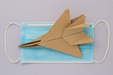 Origami kağıt uçak modeli. Seçici odaklanma. Tıbbi bir maskenin arka planına karşı. Covid-19 Kilitleme Hobisi