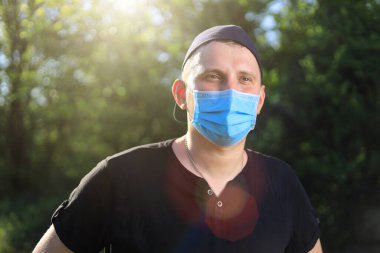 Günlük giysiler ve tıbbi maske takan beyaz bir genç ya da yetişkin adam şehir dışında doğanın tadını çıkarıyor. Ayarlanmış arkaplan