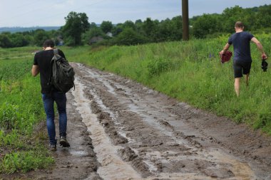 Köylüler yağmurdan sonra ıslak bir toprak yolda eve dönmeye çalışırlar. Yol eksikliği sorunu..