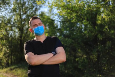 Günlük giysiler ve tıbbi maske takmış beyaz bir genç ya da yetişkin bir adam şehir parkında dinleniyor..