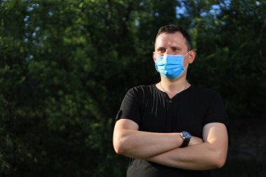 Günlük giysiler ve tıbbi maske takan beyaz bir genç ya da yetişkin adam şehir dışında doğanın tadını çıkarıyor. Ayarlanmış arkaplan