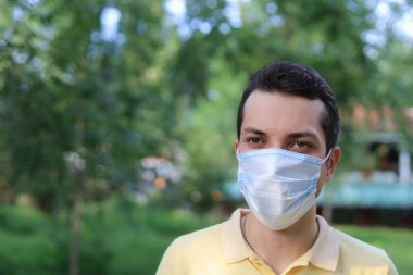 Tıbbi maske takmış, şehir ortamının bulanık arka planında yüzünü koruyan beyaz bir adamın yaşam tarzı portresi.