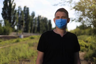 Günlük giysiler ve tıbbi maske takan beyaz bir genç ya da yetişkin adam şehir dışında doğanın tadını çıkarıyor. Ayarlanmış arkaplan