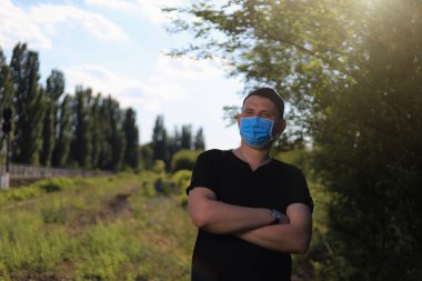 Günlük giysiler ve tıbbi maske takan beyaz bir genç ya da yetişkin adam şehir dışında doğanın tadını çıkarıyor. Ayarlanmış arkaplan
