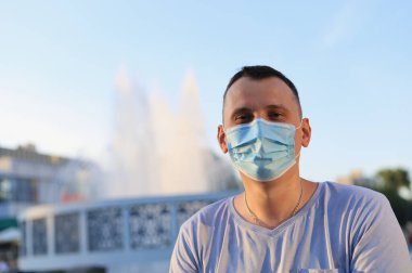 Mutlu gülümseyen genç turist günlük giysiler içinde ve tıbbi bir maske takarak covid-19 salgını sırasında yüzünü koruyor..