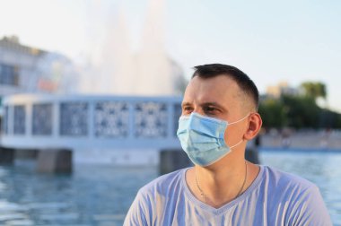 Mutlu gülümseyen genç turist günlük giysiler içinde ve tıbbi bir maske takarak covid-19 salgını sırasında yüzünü koruyor..