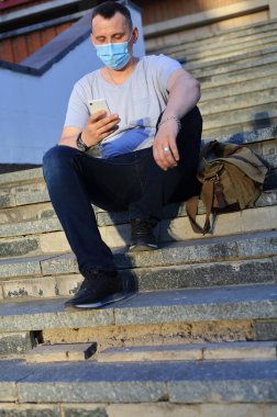 Mutlu gülümseyen genç turist günlük giysiler içinde ve tıbbi bir maske takarak covid-19 salgını sırasında yüzünü koruyor..