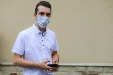 Tıbbi maske takmış, şehir ortamının bulanık arka planında yüzünü koruyan beyaz bir adamın yaşam tarzı portresi.