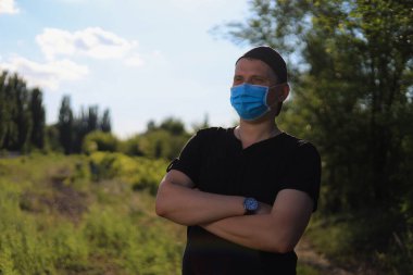 Günlük giysiler ve tıbbi maske takmış beyaz bir genç ya da yetişkin bir adam şehir parkında dinleniyor..