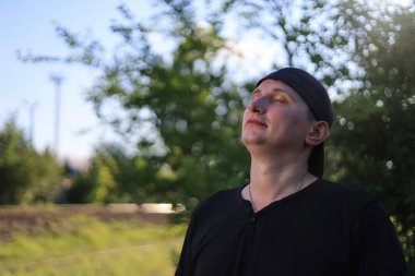 Sıradan giyinmiş beyaz bir genç ya da yetişkin bir adam yeşil bir parkta rahatça nefes alabiliyor. Mutluluk ve özgürlük kavramı.