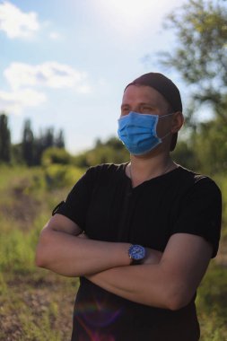 Günlük giysiler ve tıbbi maske takan beyaz bir genç ya da yetişkin adam şehir dışında doğanın tadını çıkarıyor. Ayarlanmış arkaplan