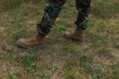 Çimlerin üzerinde duran asker çizmeleri ve kıyafetleri giymiş gerçek bir askerin bacakları. Kopyalama alanı olan arkaplan.