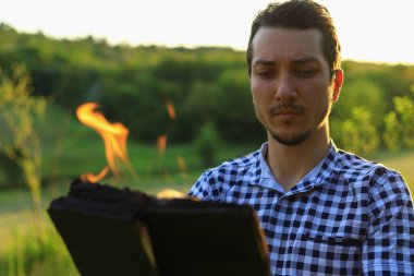 Beyaz Kafkasyalı genç adam ya da yetişkin adam bulanık orman geçmişi üzerine yanan bir kitap okuyor..