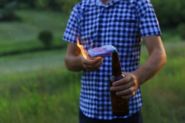 Kafkasyalı beyaz bir gencin ya da sıradan giyinen yetişkin bir adamın bulanık arka planında molotof kokteyli yakmak. Tıbbi maske fitil olarak kullanılır..