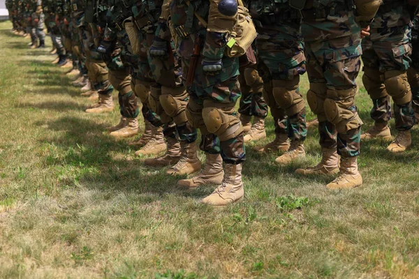Legs of real soldiers in military boots and clothes standing in formation on the grass. Background with copyspace.