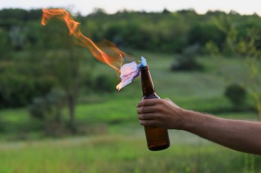 Kafkasyalı beyaz bir gencin ya da sıradan giyinen yetişkin bir adamın bulanık arka planında molotof kokteyli yakmak. Tıbbi maske fitil olarak kullanılır..