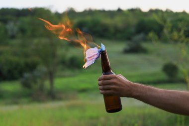 Kafkasyalı beyaz bir gencin ya da sıradan giyinen yetişkin bir adamın bulanık arka planında molotof kokteyli yakmak. Tıbbi maske fitil olarak kullanılır..