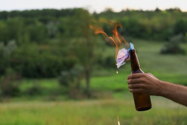 Kafkasyalı beyaz bir gencin ya da sıradan giyinen yetişkin bir adamın bulanık arka planında molotof kokteyli yakmak. Tıbbi maske fitil olarak kullanılır..