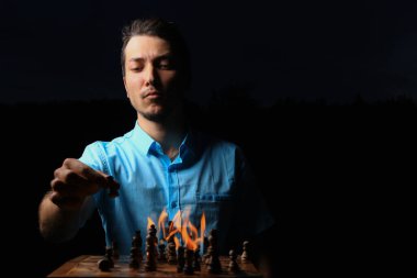 Beyaz, beyaz, genç bir adam ya da yetişkin bir adam ve yanan bir satranç tahtası. Karanlık anahtar, siyah arkaplan, seçici odak.