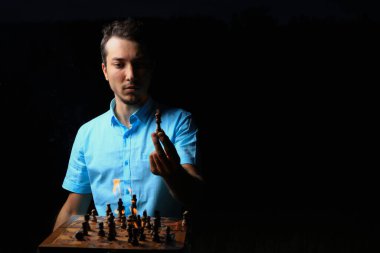 Beyaz, beyaz, genç bir adam ya da yetişkin bir adam ve yanan bir satranç tahtası. Karanlık anahtar, siyah arkaplan, seçici odak.
