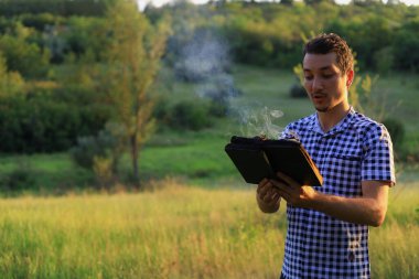 Beyaz Kafkasyalı genç adam ya da yetişkin adam bulanık orman geçmişi üzerine yanan bir kitap okuyor..