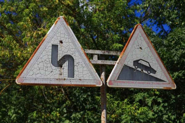 Old road signs Winding road and steep descent. Sunburned and cracked paint.