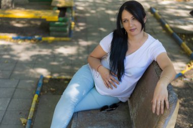 Açık renk elbiseli hamile bir kadın güneşli bir günde parkın ağaçlarının gölgesinde dinleniyor. Tonlanmış bir geçmiş. Seçici odak