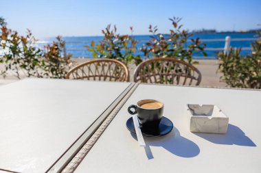 Deniz manzaralı ve açık mavi gökyüzü olan sahil kenarındaki kafe masasında Espresso bardağı..