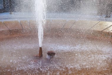 Dinamik çeşme spreyi, güneş ışığı damlacıkları ve şehir ortamında beton havza, doğal gayzer..