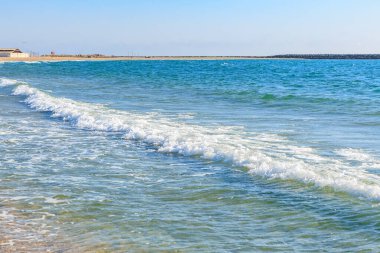 Berrak mavi suları ve yumuşak dalgaları olan sakin sahil kıyısı.