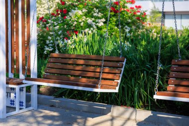 Çiçek açan bahçede kırmızı ve beyaz çiçeklerle tahta salıncak..