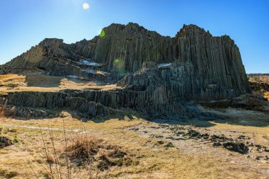 Güneşli arazide açık mavi gökyüzü altında bazalt kaya oluşumu.
