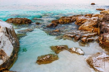 Arka planda su bulunan kayalık bir sahil. Su mavi ve kayalar beyaz.