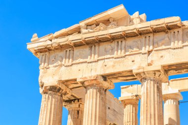 Bina, arka planda sütunları ve mavi gökyüzü olan bir tapınak. Sütunlar taştan yapılmış ve bina çok eski.