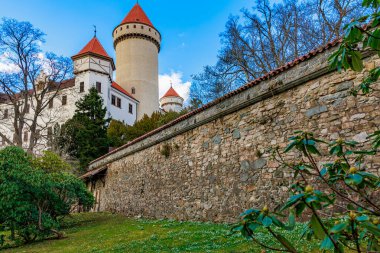 Ortaçağ taştan kalesi, yemyeşil manzaranın ortasında kırmızı çatı kuleleri..
