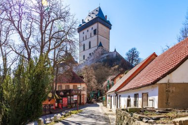 Açık bir günde küçük bir Avrupa köyünde kulesi olan tarihi gotik kale. 19 Mart 2025, Karlstejn, Çek Cumhuriyeti.