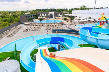 Gökkuşağı kaydırağı ve havuzu olan bir su parkı. Kaydırak çok renkli ve havuz sandalyelerle çevrili. 8 Haziran 2024 Balti Moldova