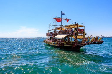 Kırmızı yelkenli ve beyaz tenteli büyük bir tekne okyanusta yüzüyor. Tekne insan kaynıyor ve teknede birkaç bayrak var. 8 Ağustos 2024 Selanik Yunanistan