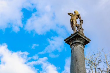 Mavi gökyüzüne ve bulutlara karşı uzun kolonda antik taş heykel. 17 Mart 2025, Konopiste Şatosu, Çek Cumhuriyeti.